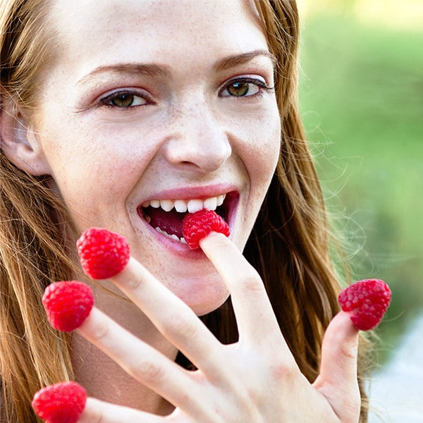 Woman eating raspberries off her fingertips