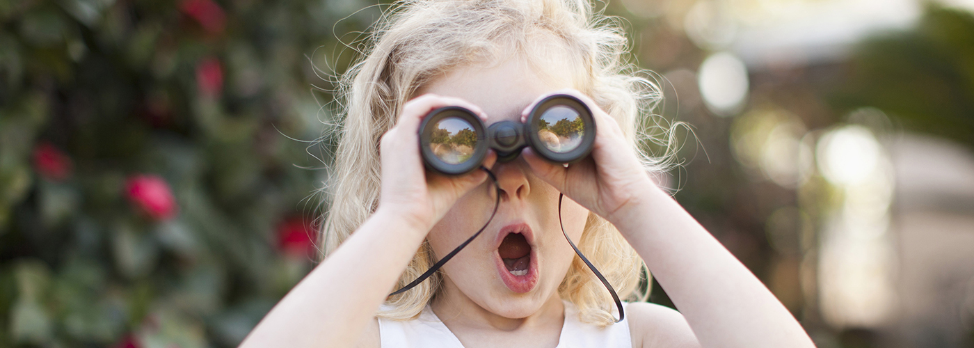 Little girl with her mouth open looking through binoculars